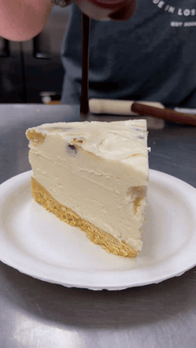 A Slice Of Cheesecake On A Paper Plate With A Person In The Background GIF