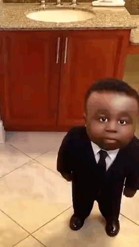 A Small Boy In A Suit And Tie Is Standing In Front Of A Bathroom Sink . GIF