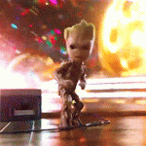A Small Figurine Of Groot Is Standing On A Table In Front Of A Fireball . GIF