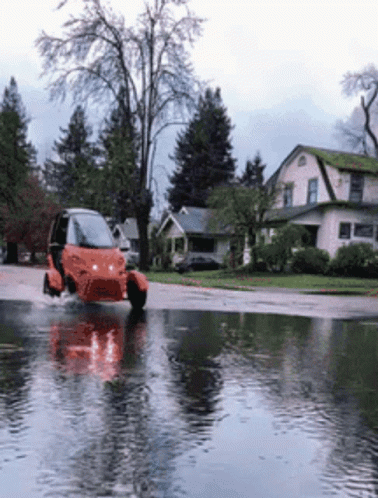 A Small Orange Vehicle Is Driving Through A Flooded Street GIF