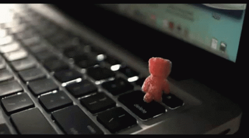 A Small Red Teddy Bear Sits On The Delete Key On A Laptop Keyboard GIF