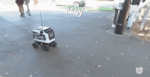 A Small White And Black Food Delivery Vehicle Is Driving Down A Street GIF