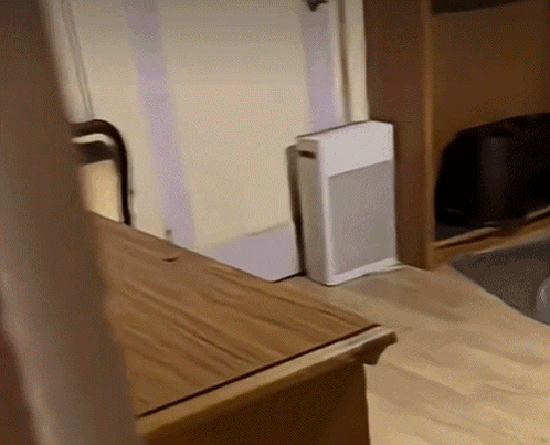 A Small White Box Is Sitting On The Floor Next To A Wooden Table GIF