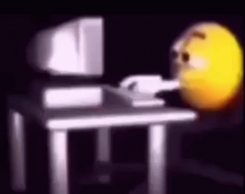 A Smiley Face Is Sitting At A Desk In Front Of A Computer Monitor . GIF