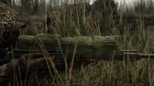 A Sniper Is Standing In The Grass With A Rifle In His Hand GIF