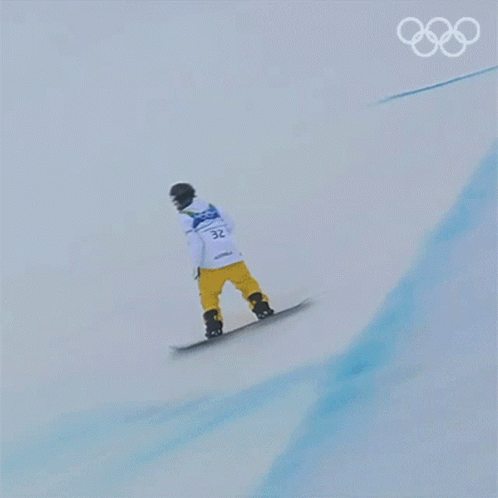 A Snowboarder Is Doing A Trick On A Snowy Slope With The Olympic Rings In The Background GIF
