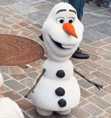 A Snowman With A Carrot Nose Is Standing On A Brick Pavement GIF