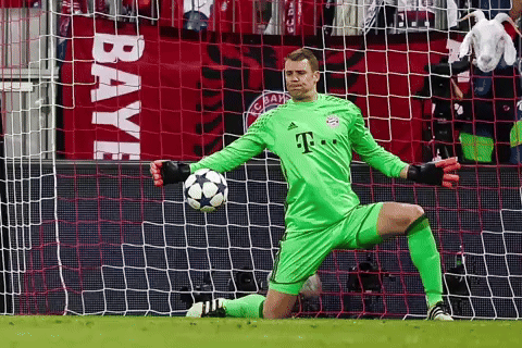a soccer goalie in a green jersey with the letter t on it is holding a soccer ball in front of a net .