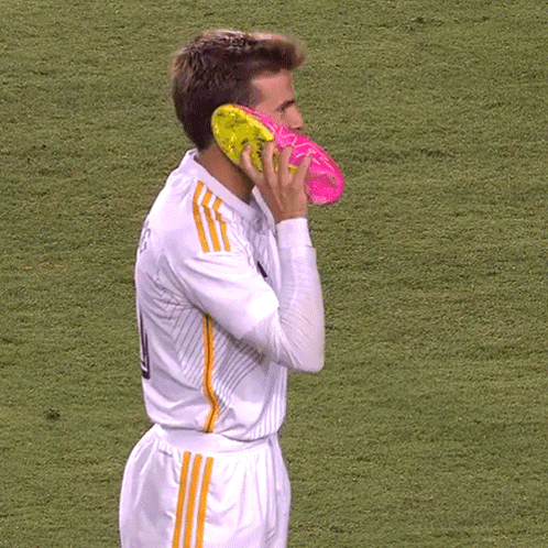 A Soccer Player Has A Pair Of Pink And Yellow Soccer Cleats On His Face GIF