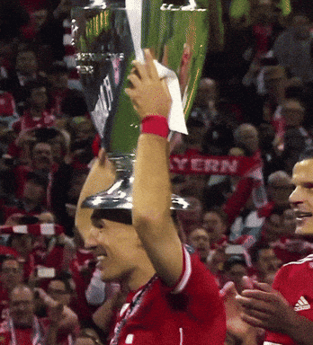 a soccer player holds up a trophy in front of a crowd with a bayern scarf behind him