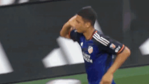 A Soccer Player In A Blue Jersey Is Standing On A Field With His Hand On His Face . GIF