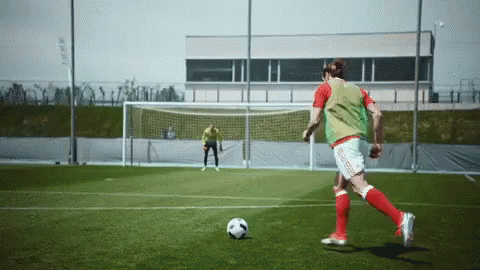 A Soccer Player In A Green Vest Kicks A Soccer Ball GIF