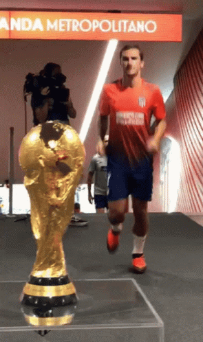A Soccer Player In A Red And Blue Uniform Is Running Towards A Trophy GIF