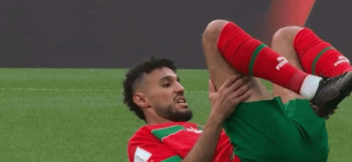 A Soccer Player In A Red And Green Uniform Stretches His Leg GIF