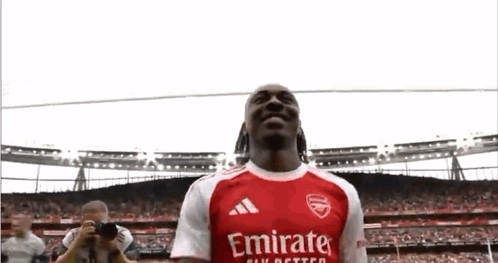 A Soccer Player In A Red And White Emirates Jersey Is Standing In Front Of A Crowd . GIF