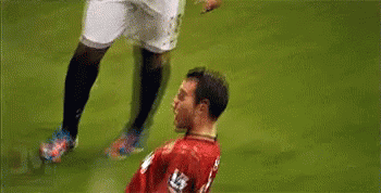 a soccer player in a red jersey is being tackled by another player on a field .