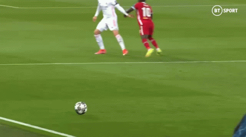 a soccer player in a red jersey is kicking a soccer ball while another player tries to stop him .