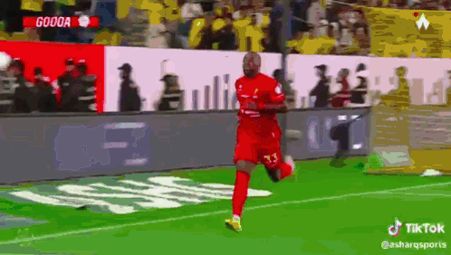a soccer player in a red jersey is running on the field with a crowd behind him