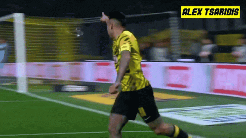 A Soccer Player In A Yellow Jersey Is Running On The Field With Alex Tsaridis In The Background GIF