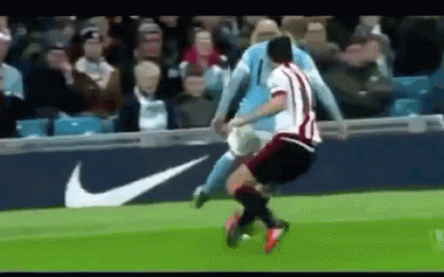 A Soccer Player Is Being Tackled By Another Player On A Soccer Field . GIF