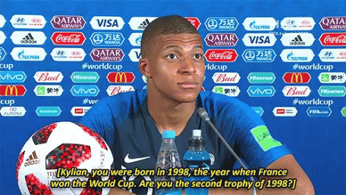 A Soccer Player Is Giving A Press Conference With A Bottle Of Water And A Soccer Ball Behind Him GIF