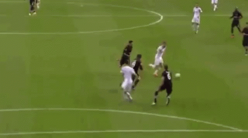 A Soccer Player Is Jumping In The Air To Score A Goal While A Goalkeeper Is Laying On The Field . GIF