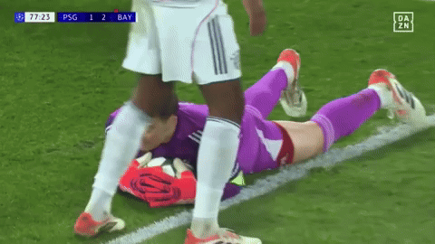 a soccer player is laying on the field while another player kicks him .