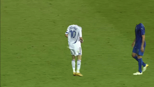 A Soccer Player Is Laying On The Ground While Another Player Runs Towards Him GIF