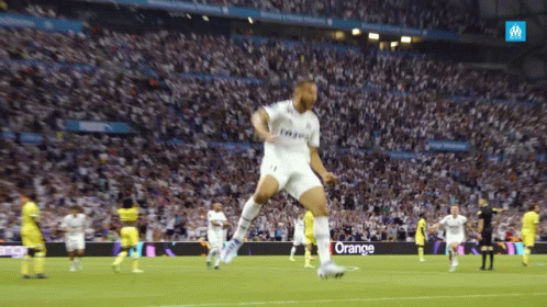 A Soccer Player Jumps In The Air In Front Of A Crowd With An Orange Sign In The Background GIF