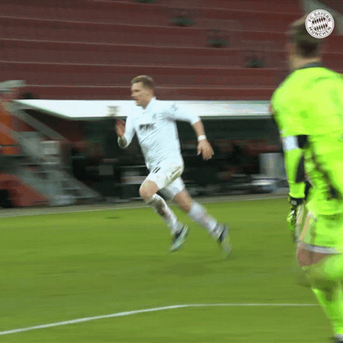 a soccer player running on a field with a bayern munich logo on the top