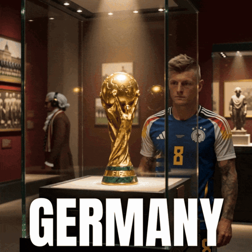 A Soccer Player Stands In Front Of A Fifa Trophy In A Glass Case GIF