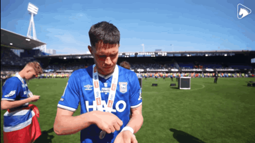 a soccer player wearing a blue halo shirt looks at his watch