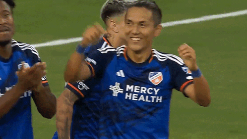 A Soccer Player Wearing A Blue Mercy Health Jersey Is Being Hugged By Another Player . GIF