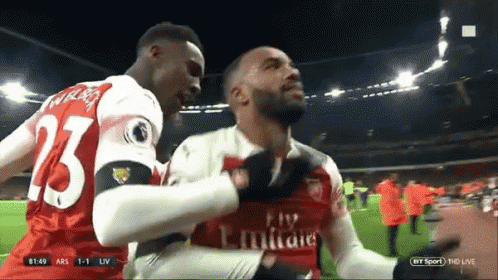 A Soccer Player Wearing A Fly Emirates Jersey Is Being Hugged By Another Player GIF