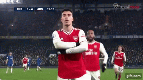 a soccer player wearing a fly emirates jersey stands on the field with his arms crossed