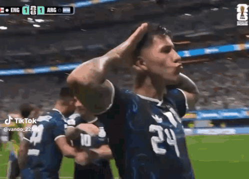 a soccer player wearing a number 24 jersey is standing on a field with his hands on his head .