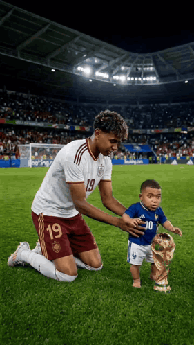 A Soccer Player With The Number 19 On His Jersey Is Kneeling Down With A Baby GIF