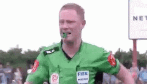 A Soccer Referee Is Wearing A Green Shirt With A Fifa Logo On It And Has A Green Object In His Mouth . GIF