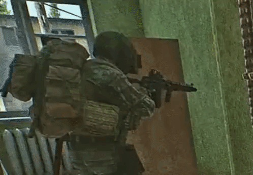 A Soldier Is Holding A Gun In A Room With A Backpack . GIF
