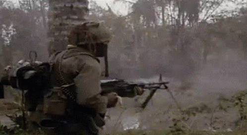 A Soldier Is Holding A Machine Gun In A Field With Trees In The Background GIF