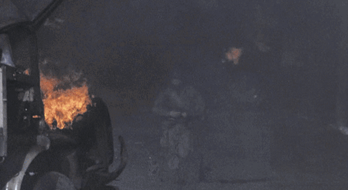A Soldier Stands In Front Of A Truck That Is On Fire GIF