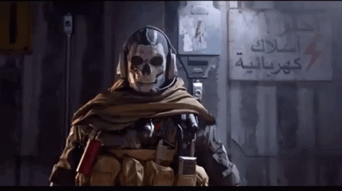 a soldier with a skull on his head is standing in front of a wall with arabic writing