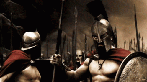 A Spartan Soldier Is Holding A Spear And Shield While Standing Next To Another Spartan Soldier GIF