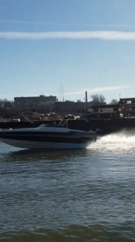 A Speed Boat Is Going Through The Water With A City In The Background GIF