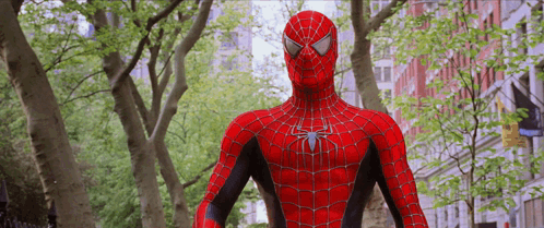 A Spider Man Is Standing In Front Of Trees And Buildings GIF