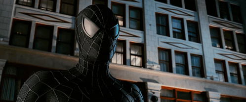 A Spider Man Stands In Front Of A Building GIF