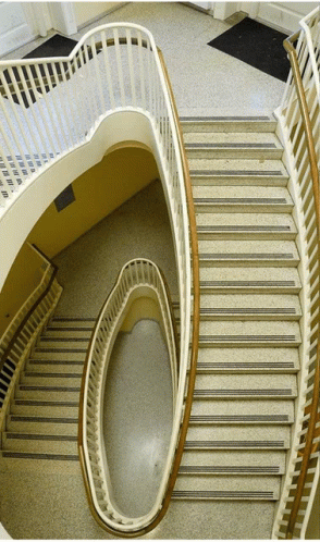 A Spiral Staircase With A White Railing And A Black Mat On The Ground GIF