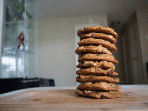 A Stack Of Chocolate Chip Cookies On A Wooden Surface GIF
