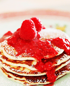 A Stack Of Pancakes Topped With Raspberries And Powdered Sugar GIF