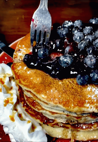 A Stack Of Pancakes With Blueberries On Top And Whipped Cream On The Side GIF